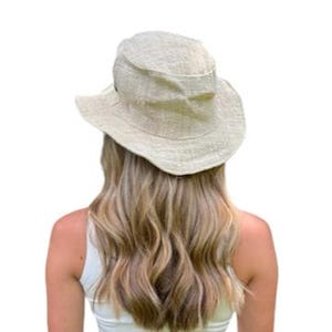 May include: A light beige sun hat with a wide brim. The hat is made of a textured fabric and has a slightly rounded crown. The hat is worn by a person wearing a white tank top.