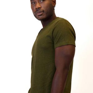 May include: A short-sleeved V-neck t-shirt in a solid olive green color. The garment features a simple, clean design with a standard fit, short sleeves, and a V-shaped neckline, crafted from a soft, textured fabric in a deep, earthy tone.