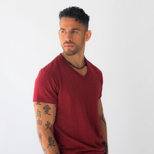 May include: A short-sleeved, deep red V-neck t-shirt with a textured fabric finish. The shirt features a classic cut with a clean neckline and hem, providing a solid color base. The garment is presented in a simple, straightforward style.