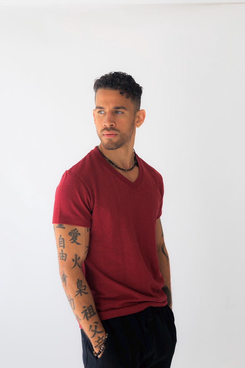 May include: A short-sleeved, deep red V-neck t-shirt with a textured fabric finish. The shirt features a classic cut with a clean neckline and hem, providing a solid color base. The garment is presented in a simple, straightforward style.