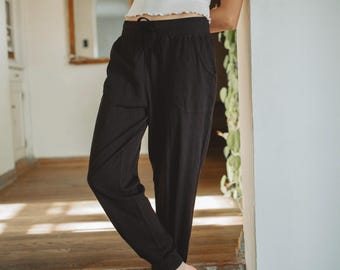 May include: A white ribbed tank top with a scalloped hem paired with black drawstring joggers featuring an elastic waistband and side pockets. The joggers have a relaxed fit through the legs and tapered cuffs at the ankles, creating a casual look.