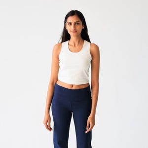 May include: A white sleeveless crop top with a round neckline paired with high-waisted navy blue flared pants. The top is fitted and ends above the waist, while the pants feature a wide waistband and a straight-leg cut that flares at the bottom.