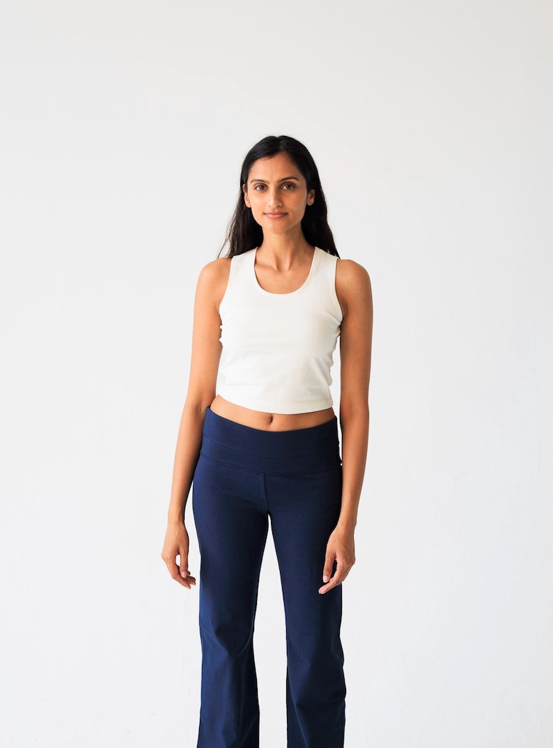 May include: A white sleeveless crop top with a round neckline paired with high-waisted navy blue flared pants. The top is fitted and ends above the waist, while the pants feature a wide waistband and a straight-leg cut that flares at the bottom.