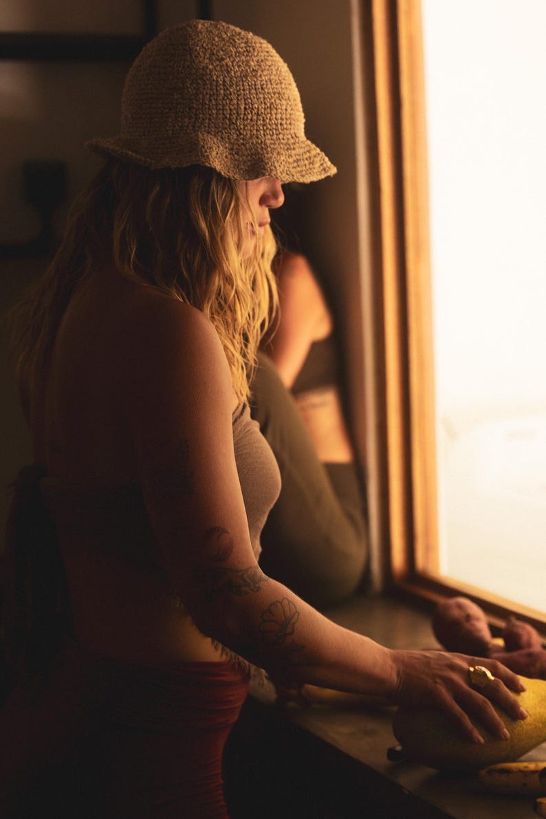 May include: A beige crochet bucket hat with a textured, woven pattern and a slightly flared brim. The hat features a natural, earthy tone and a structured yet flexible design, providing a simple and functional head covering for various outdoor activities.