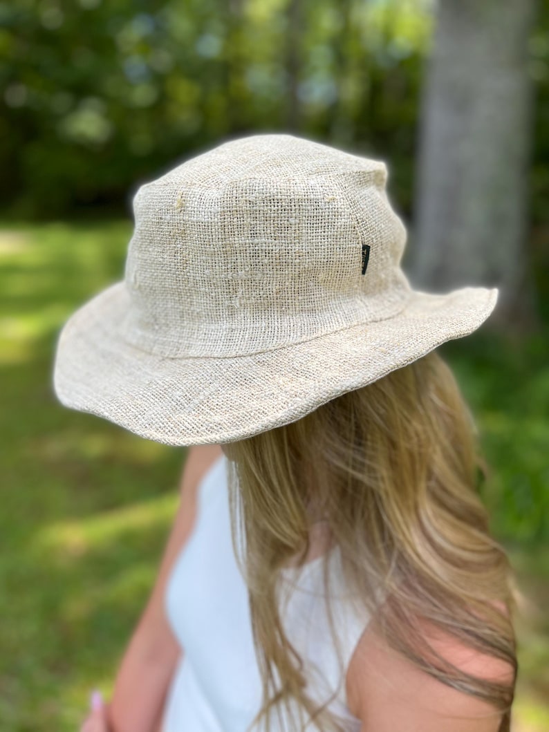 May include: A beige, wide-brimmed sun hat made of woven material. The hat has a slightly crumpled appearance and a small black tag on the side. The hat is designed to provide shade from the sun.