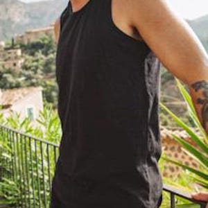 Puede incluir: Una camiseta de tirantes negra lisa sin mangas con un cuello redondo cl&aacute;sico y tirantes anchos. La prenda est&aacute; confeccionada con un tejido liso y opaco con un dobladillo recto que llega hasta la cadera, ofreciendo una silueta sencilla y limpia.