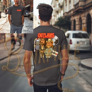 Puede incluir: Camiseta gris oscuro con la palabra "OUTLAWS" en rojo en la parte delantera y trasera. La parte trasera presenta una ilustración de dibujos animados de tres hombres, una gramola, un disco de vinilo y una cinta de casete. La parte delantera de la camiseta tiene la palabra "OUTLAWS" en rojo.