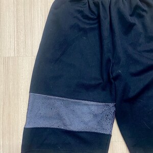 Puede incluir: Pantalones cortos deportivos negros con una franja de puntos blancos en el muslo. Los pantalones cortos tienen una cintura el&aacute;stica. La tela parece ser un material transpirable, adecuado para deportes o uso casual.
