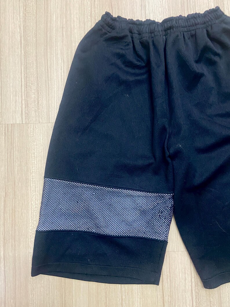 Puede incluir: Pantalones cortos deportivos negros con una franja de puntos blancos en el muslo. Los pantalones cortos tienen una cintura el&aacute;stica. La tela parece ser un material transpirable, adecuado para deportes o uso casual.