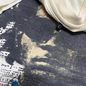 K&ouml;nnte beinhalten: Ein wei&szlig;es T-Shirt mit einem schwarz-wei&szlig;en Grafikdruck eines Gesichts. Der Grafikdruck hat einen abgenutzten Look. Das T-Shirt hat ein Gr&ouml;&szlig;enetikett mit der Aufschrift "L" am Kragen.