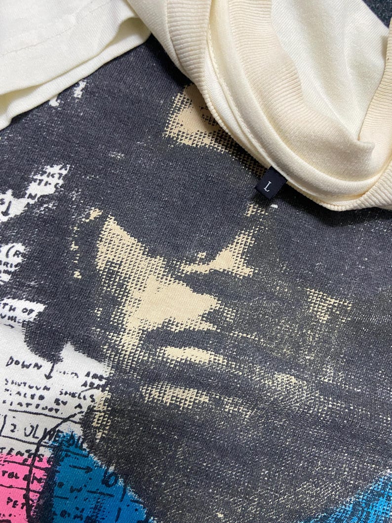 K&ouml;nnte beinhalten: Ein wei&szlig;es T-Shirt mit einem schwarz-wei&szlig;en Grafikdruck eines Gesichts. Der Grafikdruck hat einen abgenutzten Look. Das T-Shirt hat ein Gr&ouml;&szlig;enetikett mit der Aufschrift "L" am Kragen.