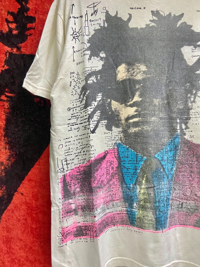 K&ouml;nnte beinhalten: Wei&szlig;es T-Shirt mit einem Schwarzwei&szlig;portr&auml;t eines Mannes mit einem blauen und rosa Design. Das Shirt hat handschriftlichen Text, darunter "Malcolm X" und "Rocket Ship".