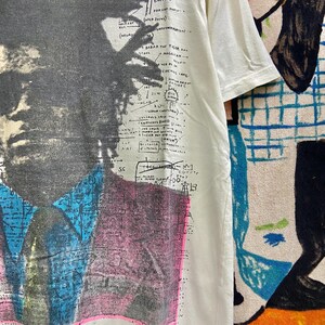 K&ouml;nnte beinhalten: Ein wei&szlig;es T-Shirt mit einem Schwarzwei&szlig;bild von Malcolm X. Das Shirt hat ein grafisches Design mit dem Text "The Riche Me of Potoss" und "Babar the Ticlan Bag".