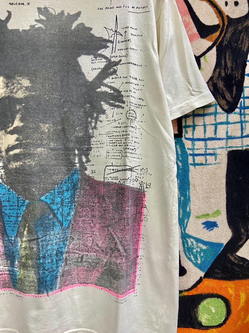 K&ouml;nnte beinhalten: Ein wei&szlig;es T-Shirt mit einem Schwarzwei&szlig;bild von Malcolm X. Das Shirt hat ein grafisches Design mit dem Text "The Riche Me of Potoss" und "Babar the Ticlan Bag".