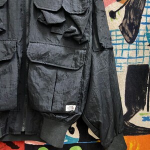 Peut inclure: Veste noire en nylon avec plusieurs poches avant et une fermeture &eacute;clair. La veste pr&eacute;sente un poignet c&ocirc;tel&eacute; et une petite &eacute;tiquette blanche avec un logo. Design d&eacute;contract&eacute; et utilitaire.