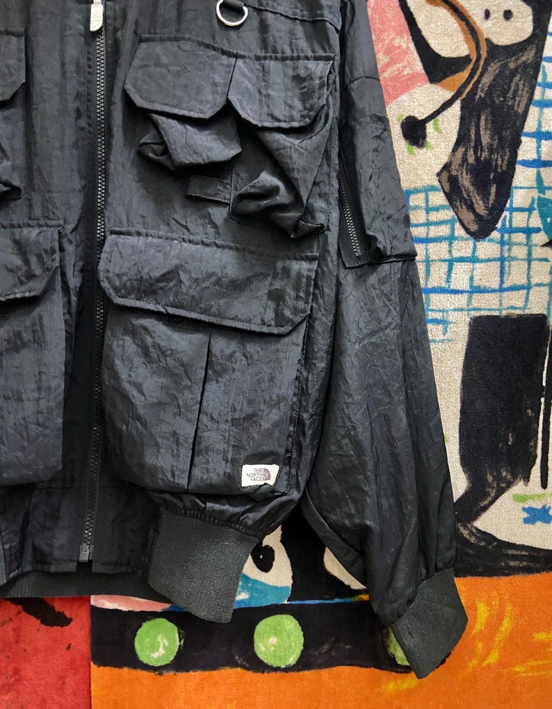 Peut inclure: Veste noire en nylon avec plusieurs poches avant et une fermeture &eacute;clair. La veste pr&eacute;sente un poignet c&ocirc;tel&eacute; et une petite &eacute;tiquette blanche avec un logo. Design d&eacute;contract&eacute; et utilitaire.