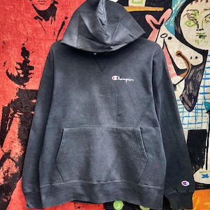 Puede incluir: Una sudadera con capucha Champion gris oscuro con un bolsillo delantero y una capucha. El logotipo de Champion está bordado en blanco, rojo y azul en el pecho. El logotipo de Champion también está en la manga izquierda.