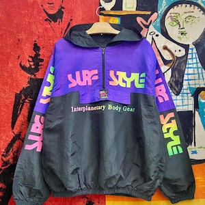 May include: A vintage black, purple, and neon-colored windbreaker jacket with the words "SURF STYLE" across the chest. The jacket has a hood, a front zipper, and the text "Interplanetary Body Gear" below the chest.