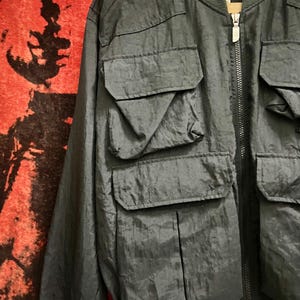 Peut inclure: Veste de bombardier noire avec plusieurs poches avant et une fermeture &eacute;clair. La veste porte le nom de la marque "The North Face" sur le col. La veste a un col et des poignets c&ocirc;tel&eacute;s. Le tissu est l&eacute;g&egrave;rement brillant.