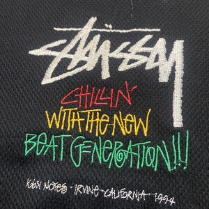 Puede incluir: Tela negra con el logotipo de Stussy bordado en blanco y texto colorido. El texto dice "Chillin' With The New Beat Generation!!!" e "Irvine California 1994".