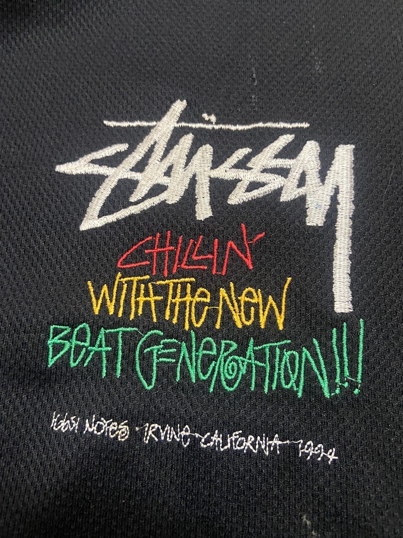 Puede incluir: Tela negra con el logotipo de Stussy bordado en blanco y texto colorido. El texto dice "Chillin' With The New Beat Generation!!!" e "Irvine California 1994".