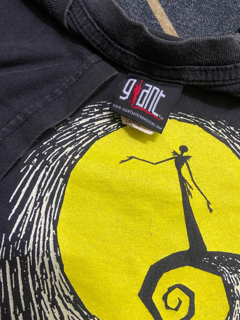 May include: Black t-shirt featuring a graphic of a character standing in front of a yellow moon. The design is in white and black. The tag reads "Giant" and "Large".