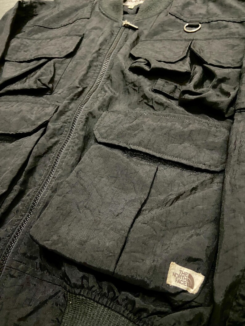 Peut inclure: Veste de bombardier noire avec plusieurs poches avant et une fermeture &eacute;clair. La veste pr&eacute;sente un col et des poignets c&ocirc;tel&eacute;s, ainsi qu'un petit &eacute;cusson logo sur le devant. La veste est en tissu textur&eacute;.