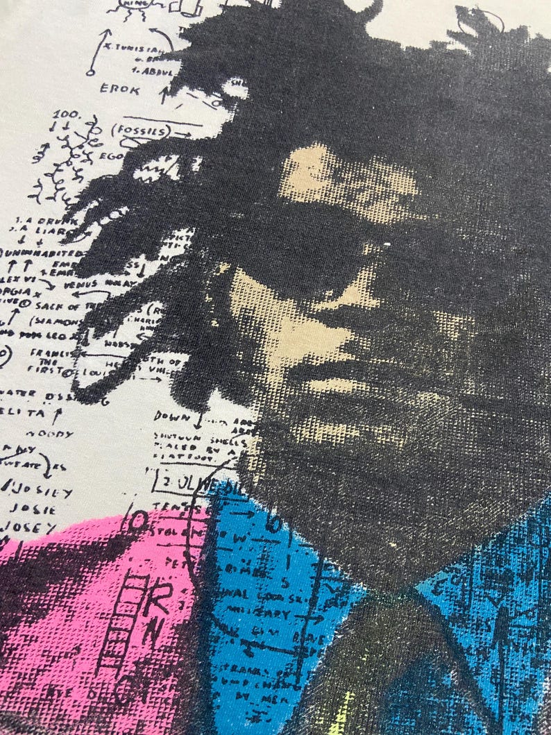 K&ouml;nnte beinhalten: Ein Vintage-T-Shirt in Wei&szlig; mit einem Schwarzwei&szlig;-Portr&auml;t einer Person. Das Portr&auml;t ist von einer bunten Karte mit handschriftlichem Text und Pfeilen umgeben. Der Text enth&auml;lt "100.", "EROK", "(FOSSILS)", "EGO", "A LIAR", "UNINABITED", "LEX VI VEMUS", "PGIA X", "HIVE SACK OF T", "T (SHAMONS", "G", "FRANCIS", "THE", "HO", "FIRSTO LOUIS", "ELITA", "22", "ETH OF", "MA", "DOWN", "A", "10000", "SHUTOUN SHELLS", "12 OLIVE DIL", "JOSILY", "JOSIE", "JOSEY", "TENS", "STAL", "M", "PET", "M", "R", "5", "ZARY".