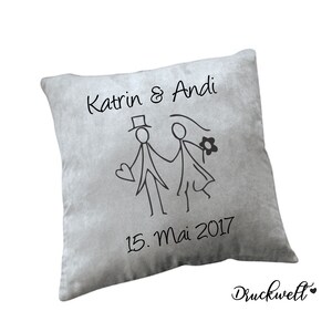 May include: Grey throw pillow with a black stick figure illustration of a bride and groom with the text "Katrin & Andi 15. Mai 2017" printed on it.