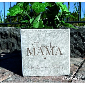 Könnte beinhalten: Ein quadratischer, hellgrauer Betonblumentopf mit den Worten "Danke MAMA" und "Alles Liebe zum Muttertag" in brauner Schrift. Der Topf ist mit grünen Blättern gefüllt. Der Topf steht auf einer Steinoberfläche.