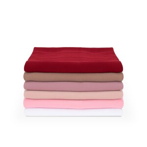 May include: Stack of five fabric squares in various shades of pink, red, and brown. The fabric is smooth and has a slight sheen.