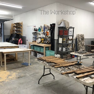 May include: A workshop with a white painted wall and a sign that reads "The Workshop". There are several tables with wooden planks on them. The workshop is well-equipped with tools and supplies.