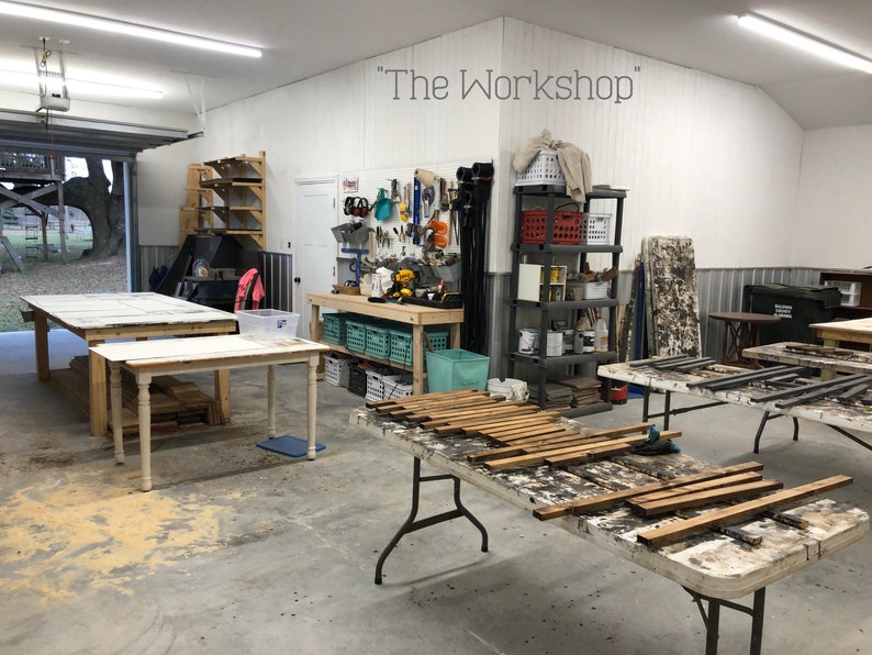 May include: A workshop with a white painted wall and a sign that reads "The Workshop". There are several tables with wooden planks on them. The workshop is well-equipped with tools and supplies.