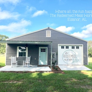 May include: A gray building with a white door and a garage door that says "a redeemed mess" in white lettering. The building has a covered porch with two white rocking chairs.