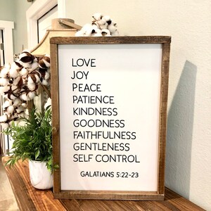 May include: A framed wood sign with white background and black text. The text reads "Love, Joy, Peace, Patience, Kindness, Goodness, Faithfulness, Gentleness, Self Control, Galatians 5:22-23".