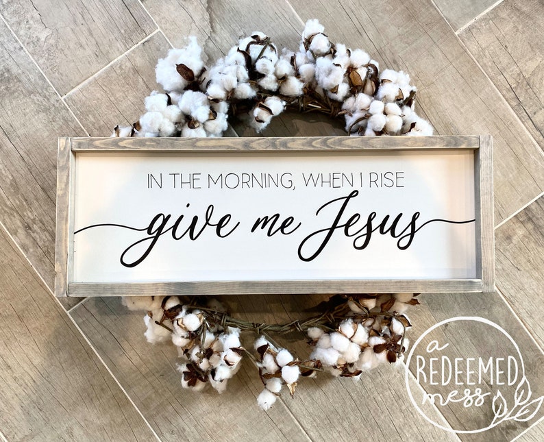 May include: A white wooden sign with a gray frame, featuring the text "In the morning, when I rise give me Jesus".