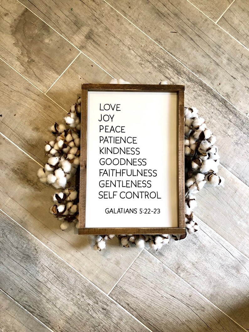 May include: A white wooden sign with black text listing the fruits of the spirit: love, joy, peace, patience, kindness, goodness, faithfulness, gentleness, and self-control. The sign also includes the scripture reference Galatians 5:22-23.