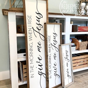 May include: Three wooden signs with the text "give me Jesus" in black cursive lettering. The signs are different sizes and have a rustic wood frame.