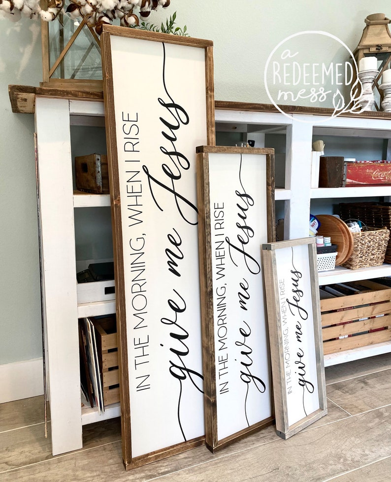 May include: Three wooden signs with the text "give me Jesus" in black cursive lettering. The signs are different sizes and have a rustic wood frame.