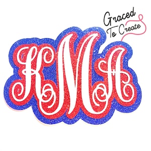 May include: A glittery monogram in red, white, and blue. The letters "KMA" are in a white, elegant script, layered over a red glitter base, and outlined with a blue glitter border. The words "Graced To Create" are in the upper right corner.