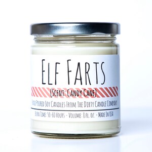 May include: A glass jar candle with a silver lid. The label reads "ELF FARTS (SCENT: CANDY CANE)" with red and white striped accents. The label also includes the text "HAND POURED SOY CANDLES FROM THE DIRTY CANDLE COMPANY BURN TIME: 50-60 HOURS - VOLUME: 8 FL. OZ. - MADE IN USA".