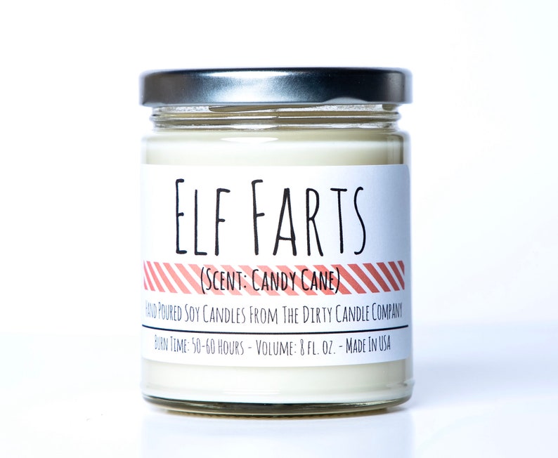 May include: A glass jar candle with a silver lid. The label reads "ELF FARTS (SCENT: CANDY CANE)" with red and white striped accents. The label also includes the text "HAND POURED SOY CANDLES FROM THE DIRTY CANDLE COMPANY BURN TIME: 50-60 HOURS - VOLUME: 8 FL. OZ. - MADE IN USA".