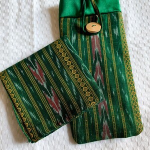 May include: A green and gold striped fabric pouch with a drawstring closure and a wooden button. The pouch is made of a soft, textured fabric and has a subtle ikat pattern.