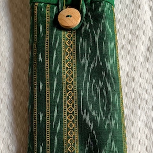 May include: A green fabric pouch with a wooden button closure. The pouch has a striped pattern with gold and white accents.