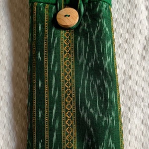May include: A green fabric pouch with a wooden button closure. The pouch has a striped pattern with gold and white accents.