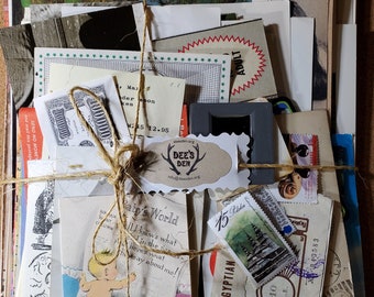 May include: A bundle of vintage ephemera tied with twine. The collection includes postcards, stamps, a slide, and a tag that reads "Dee's Den". Various colors and textures are visible, with some items featuring text and illustrations.
