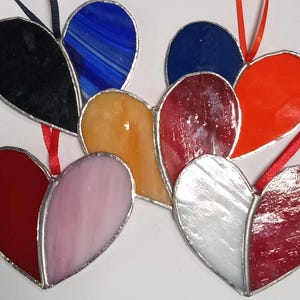 May include: A set of seven stained glass hearts in various colors, including red, blue, orange, pink, and silver. The hearts are all different sizes and shapes, and they are hanging from a string.