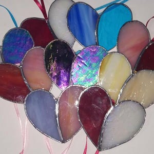 May include: A collection of stained glass hearts in various colors, including red, blue, white, and iridescent. The hearts are arranged in a fan shape and have a silver outline.