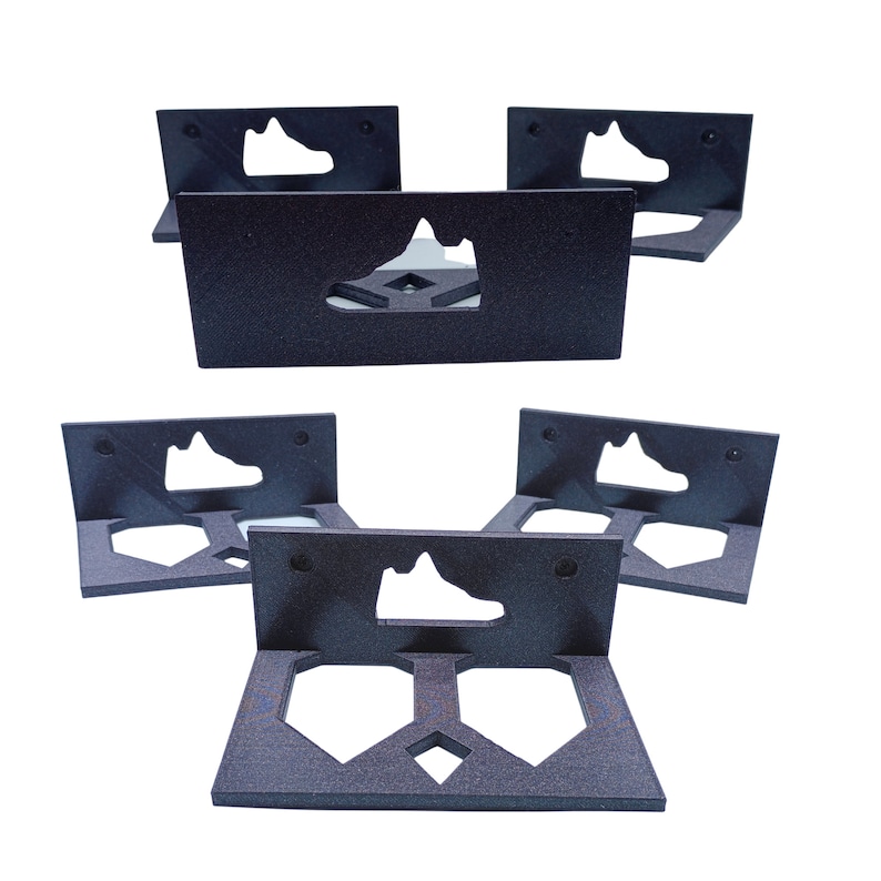 May include: Five black wall-mounted shoe holders with a cutout of a sneaker in the center. Each holder has a rectangular shape with rounded corners and a raised lip around the edge.