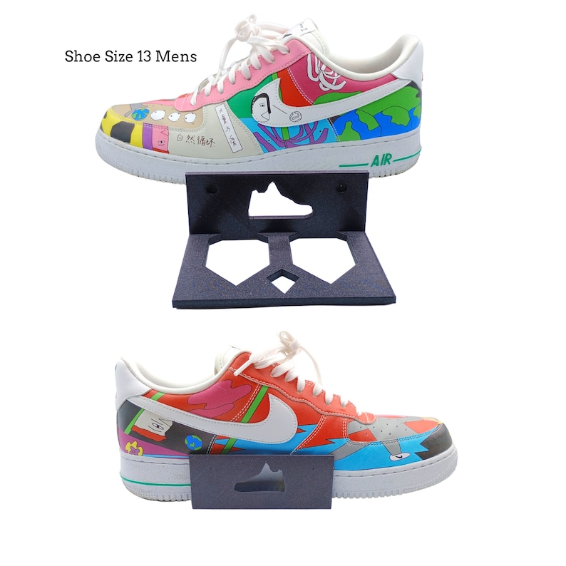 May include: Two pairs of colorful sneakers with a graphic print design, displayed on a black shoe wall mount. The sneakers are size 13.